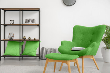 Stylish green armchair, ottoman and shelf unit in interior of living room