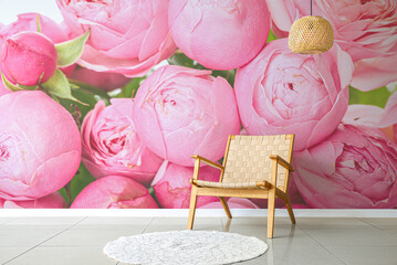 Fototapeta na wymiar Stylish wicker armchair with rug and chandelier near wall with printed flowers in room
