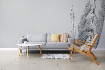 Stylish sofa with armchair and table near grey wall with printed floral decor