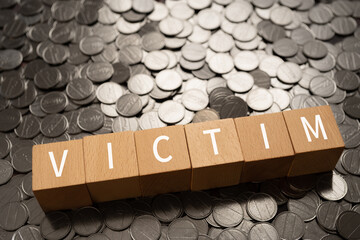 犠牲者のイメージ｜「VICTIM」と書かれた積み木とコイン