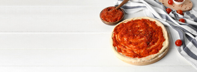 Uncooked pizza with fresh tomato sauce on white wooden background with space for text