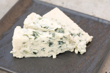 Dorblu cheese with blue and green mold veins on black serving plate. Consistency of blue cheese. Traditional antipasti, classic blue mould cheese