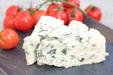 Dorblu cheese with blue and green mold veins. Classic blue mould cheese served with baby tomatoes on black plate on concrete stone table background. Traditional antipasti