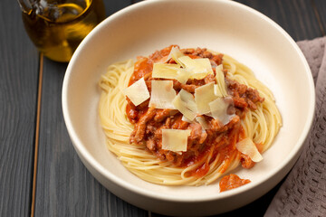 Spaghetti with bolognese sauce, parmesan cheese in a deep dish on a wooden table and a bottle of olive oil