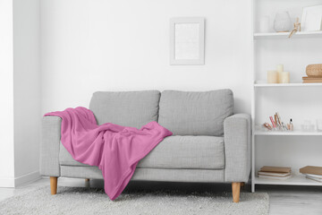 Grey sofa with plaid and shelving unit near white wall in living room
