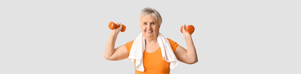Elderly woman holding dumbbells on light background with space for text