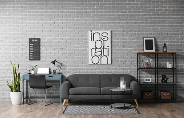 Interior of living room with modern workplace and poster with word INSPIRATION on grey brick wall