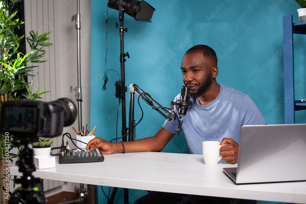 Poster vlogger adjusting volume on mixer console talking to followers in online morning show in front of li