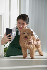 Happy groomer taking selfie with small dog after procedure to upload on page of her grooming salon