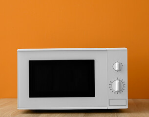Obraz premium Modern microwave oven on wooden table against orange background