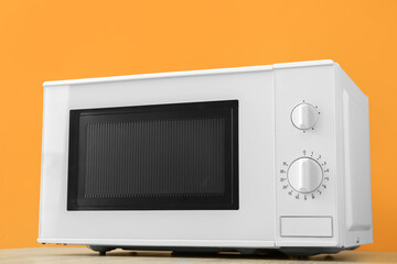 Modern microwave oven on table against orange background