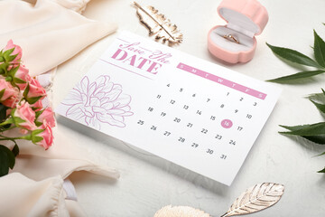 Wedding calendar with marked date, box with engagement ring and beautiful flowers on light table