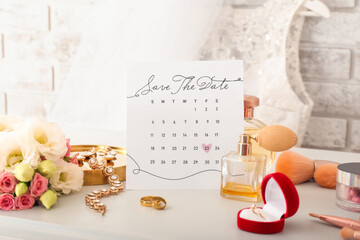 Wedding calendar with marked date, beautiful flowers and bridal accessories on table near light wall