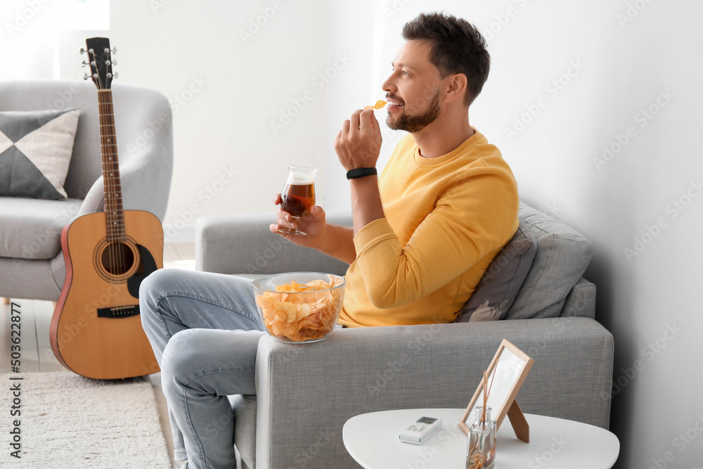 Poster Handsome man drinking beer and eating chips while watching sports at home