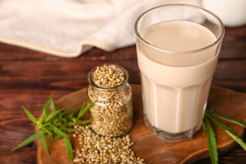 Glass of healthy hemp milk and bottle with seeds on wooden background