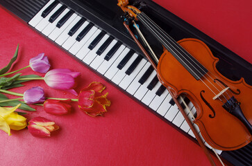 Electric guitar, synthesizer keyboard and a bouquet of tulips and lilac on a red table.