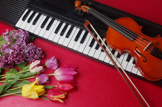 Electric guitar, synthesizer keyboard and a bouquet of tulips and lilac on a red table.