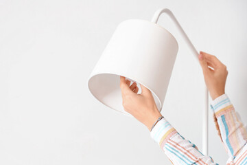 Woman changing light bulb in standard lamp near light wall, closeup