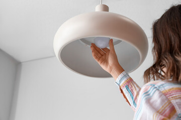 Woman changing light bulb in hanging lamp at home, closeup