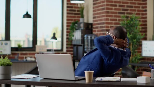 Company assistant relaxing on work timeout in startup office, relieving stress for peace of mind. Sitting with hands behind head, laid back on chair enjoying break pause at desk.