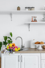 Modern light kitchen with bouquet of flowers in sink