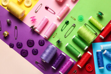 Thread spools, buttons and safety pins on color background