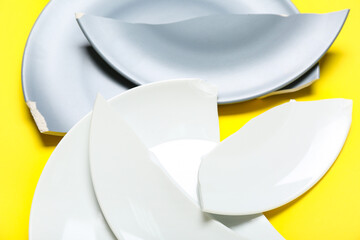 Broken ceramic plates on yellow background, closeup