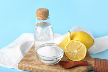 Wooden board with bottle of water, baking soda and ripe lemons on color background