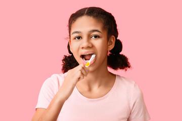 African-American teenage girl brushing teeth on pink background