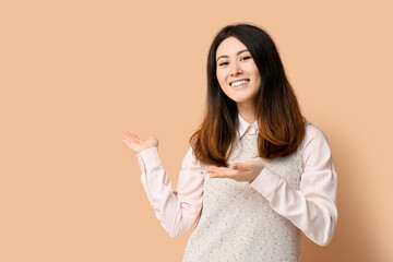 Inviting young Asian woman showing something on beige background