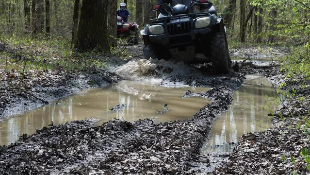 The ATV rides through puddles in the woods. Splash and mud flying in all directions. Touring rides on a quad bike. Slow motion