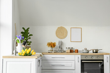 Tulips in modern sink and different utensils on kitchen counters near white wall