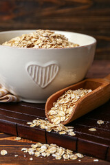 Bowl and scoop with raw oatmeal on wooden table, closeup