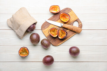 Board with delicious cut passion fruits and knife on light wooden background