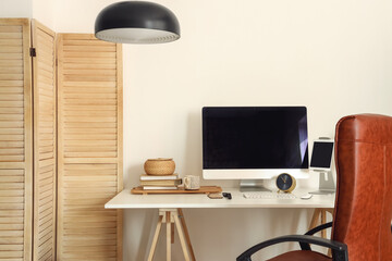 Modern computer, different gadgets and books on table near light wall