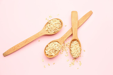Wooden spoons with raw oatmeal on pink background
