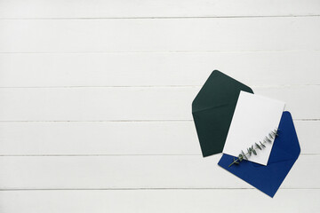 Envelopes with blank card and eucalyptus branch on white wooden background