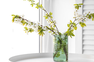 Vase with blooming tree branches on table near window, closeup
