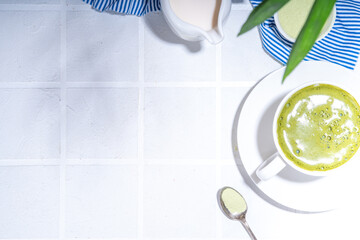 Matcha green tea latte on white concrete background with hard light, one cup of matcha drink in woman hands, top view copy space 