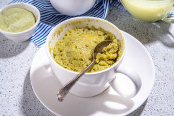 Matcha mugcake, Sweet healthy sponge cupcake biscuit in cup, simple morning breakfast baking in microwave. Organic diet mug cake brownie dessert on white tiled background copy space