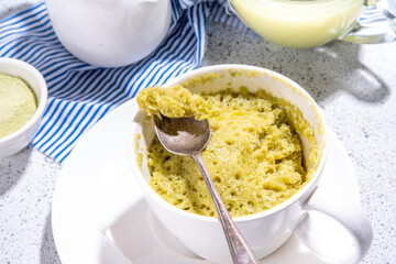Matcha mugcake, Sweet healthy sponge cupcake biscuit in cup, simple morning breakfast baking in microwave. Organic diet mug cake brownie dessert on white tiled background copy space