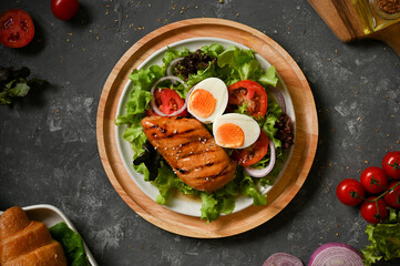 Grilled chicken breast with boiled egg and organic salad vegetables on grey table.