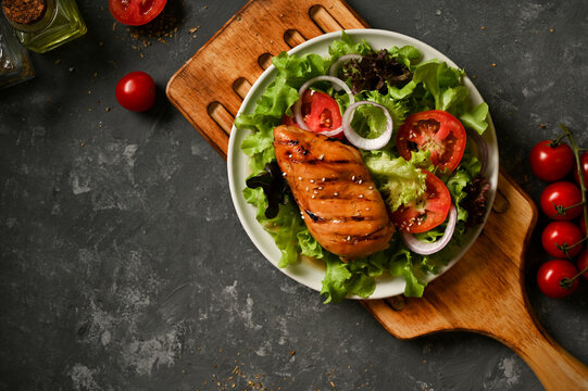Grilled chicken breast with fresh salad vegetables on a grey background