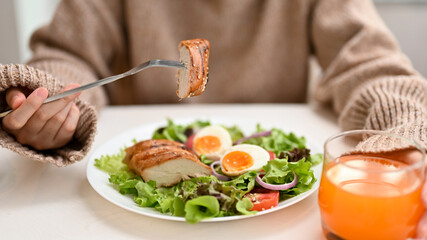 Diet woman eating a fresh healthy salad with grilled chicken breast at the table.