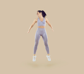 Fototapeta na wymiar Dynamic movement. Healthy sport woman with fit body doing fitness jumps isolated on beige background. Smiling young woman in sportswear doing jumping exercise. Workout sport concept. Full length.