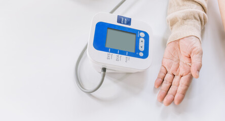 Close-up of an elderly Asian woman's hand measuring blood pressure by using automatic blood pressure monitors with a nurse. Caregivers visit homes. Home health care ideas and nursing homes.