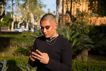 Non-binary and young person from South America is on holiday in Europe, the person is make up and wearing black clothes. He is walking around the city consulting his mobile phone. Concept of equality.