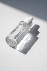 A white transparent bottle with serum in the rays of the sun.