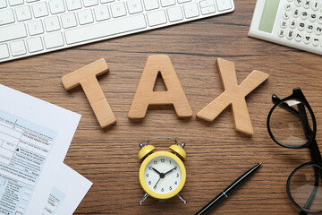 Flat lay composition with word Tax and alarm clock on wooden table