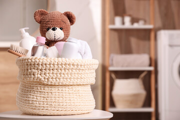 Knitted basket with baby cosmetic products, bath accessories and toy bear on white table indoors....